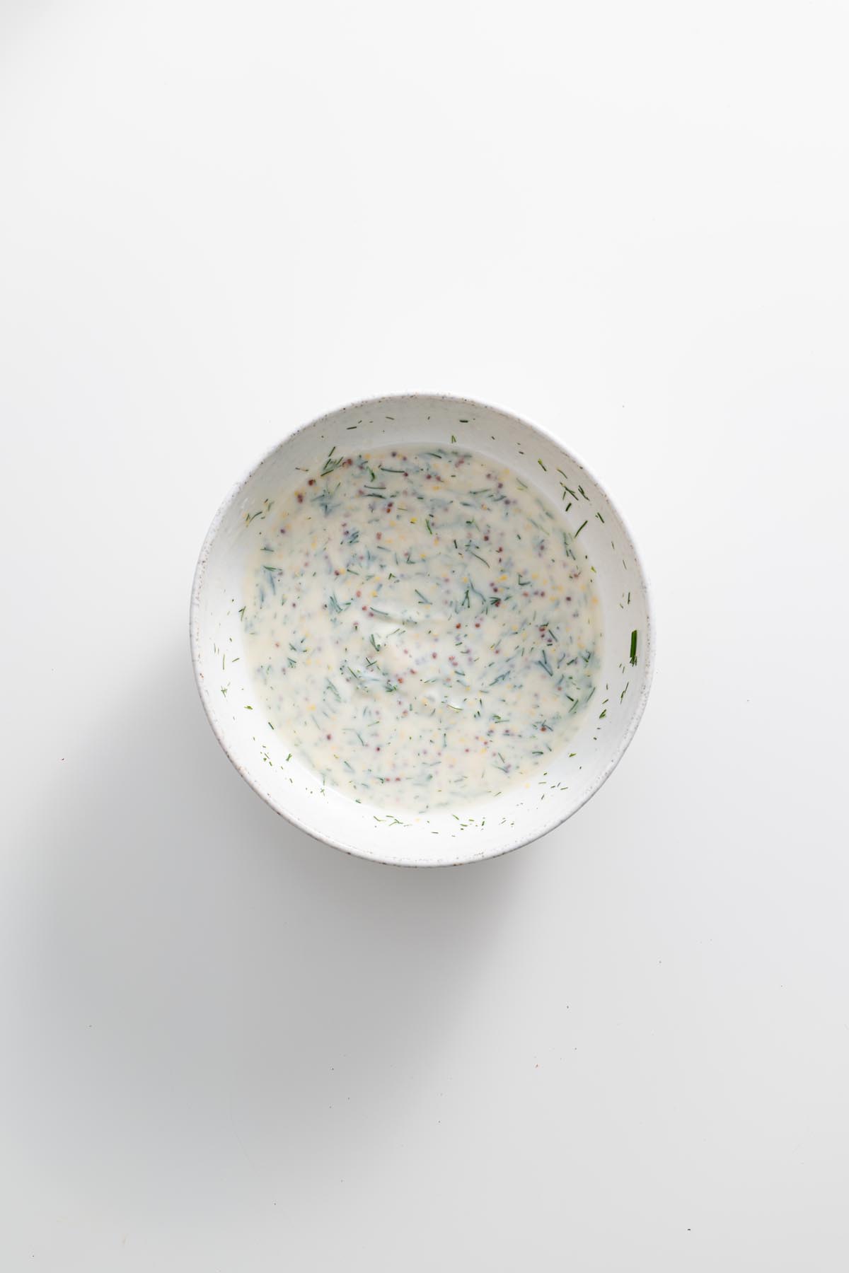 Yogurt dill sauce in a small bowl on a white surface.