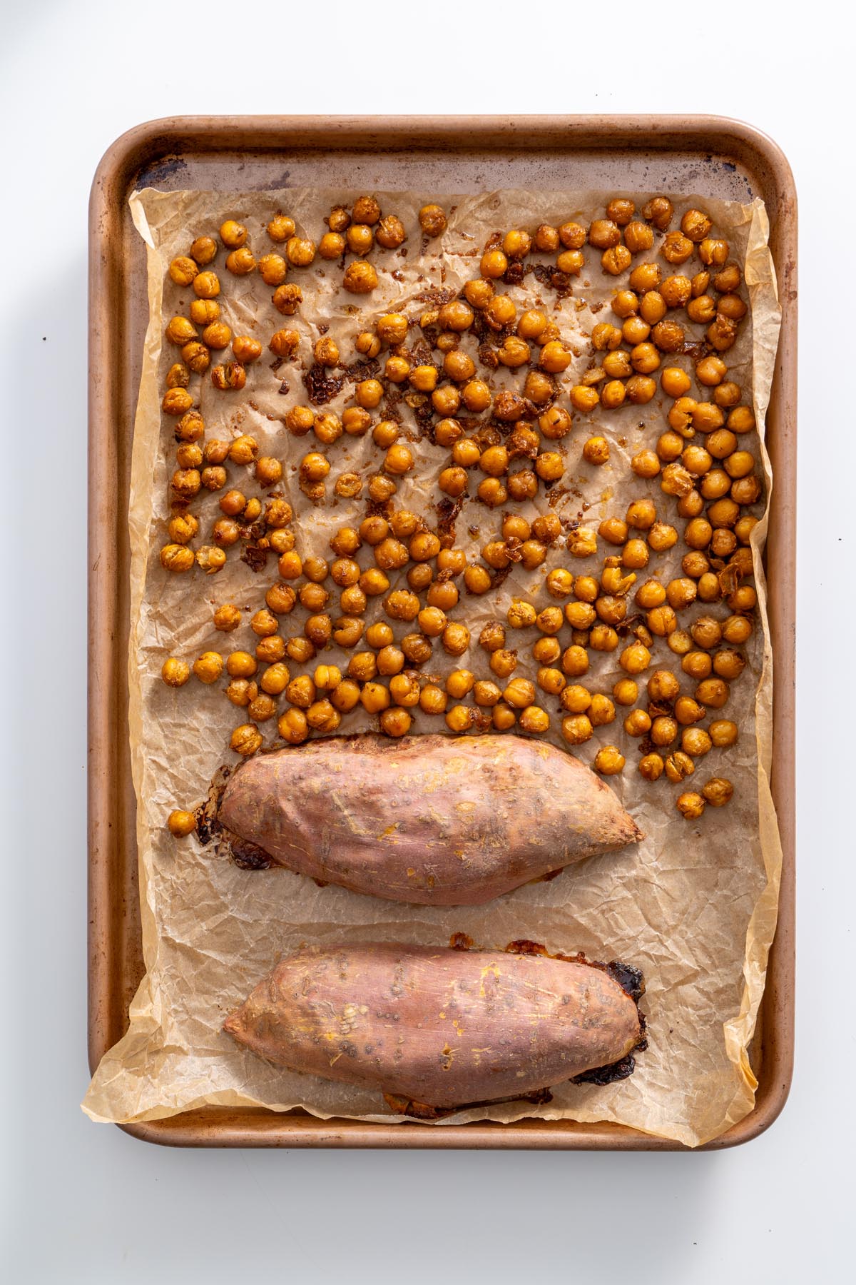 Roasted sweet potatoes and chickpeas on a parchment-lined baking tray.