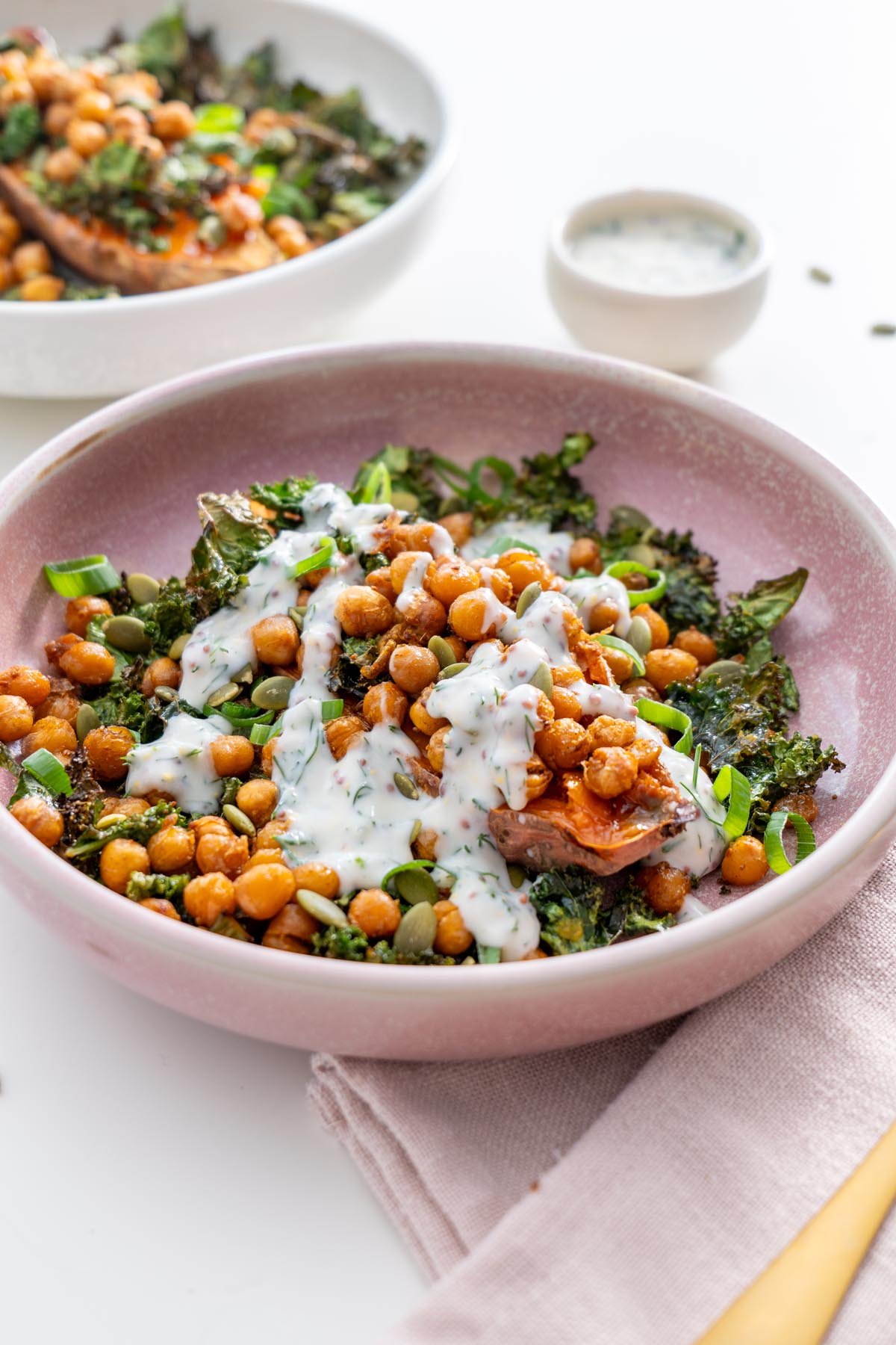 Close-up of a kale sweet potato bowl with crispy chickpeas, green onions, and yogurt dressing.