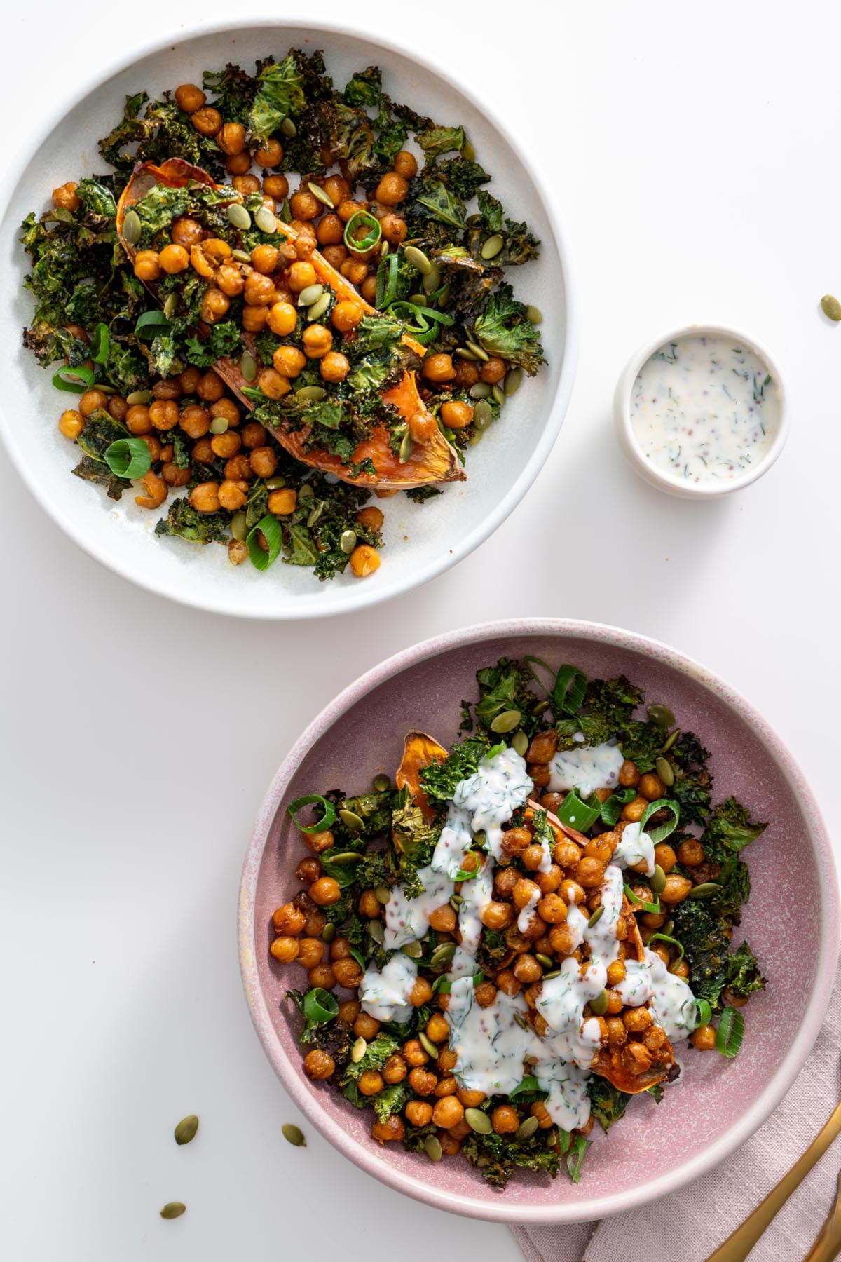 Flat lay of two kale sweet potato bowls with pumpkin seeds, chickpeas, and yogurt sauce.