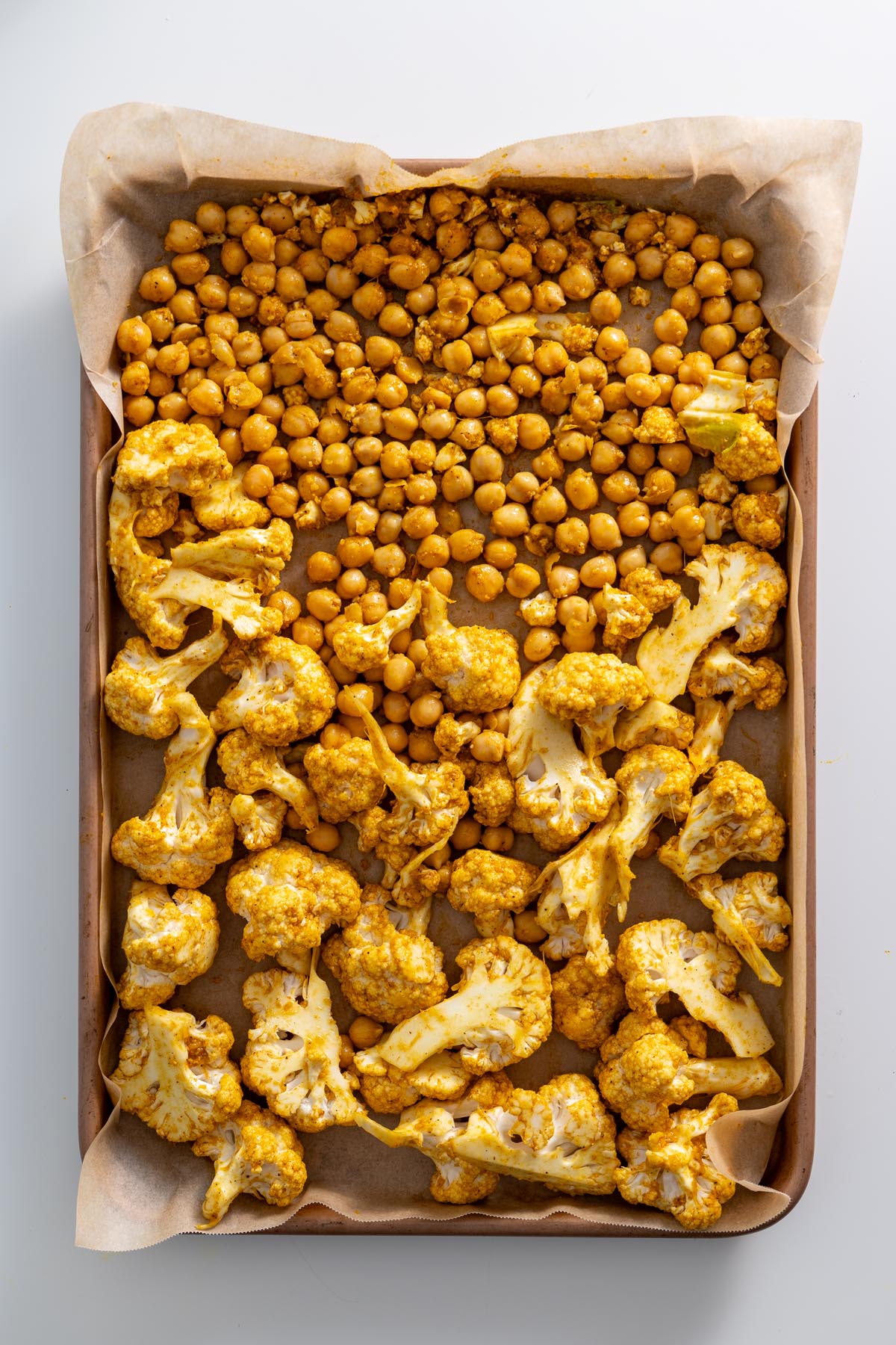 A baking tray with marinated cauliflower and chickpeas before roasting.