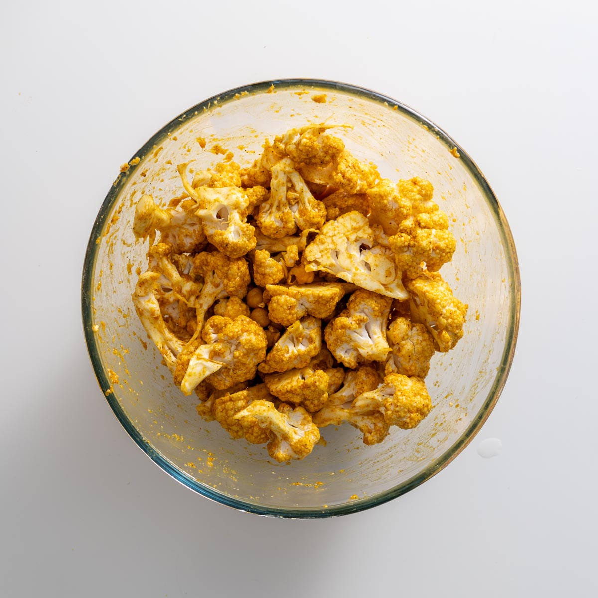 Cauliflower florets coated in a tandoori spice marinade, mixed with chickpeas in a glass bowl.