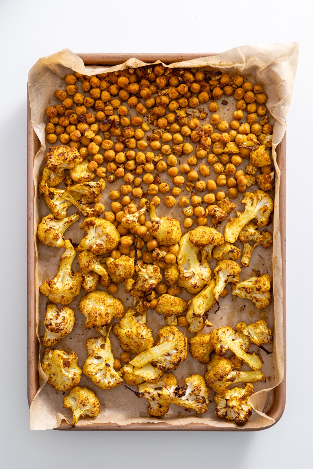 A baking tray with roasted chickpeas and cauliflower, golden brown from the tandoori spice blend.