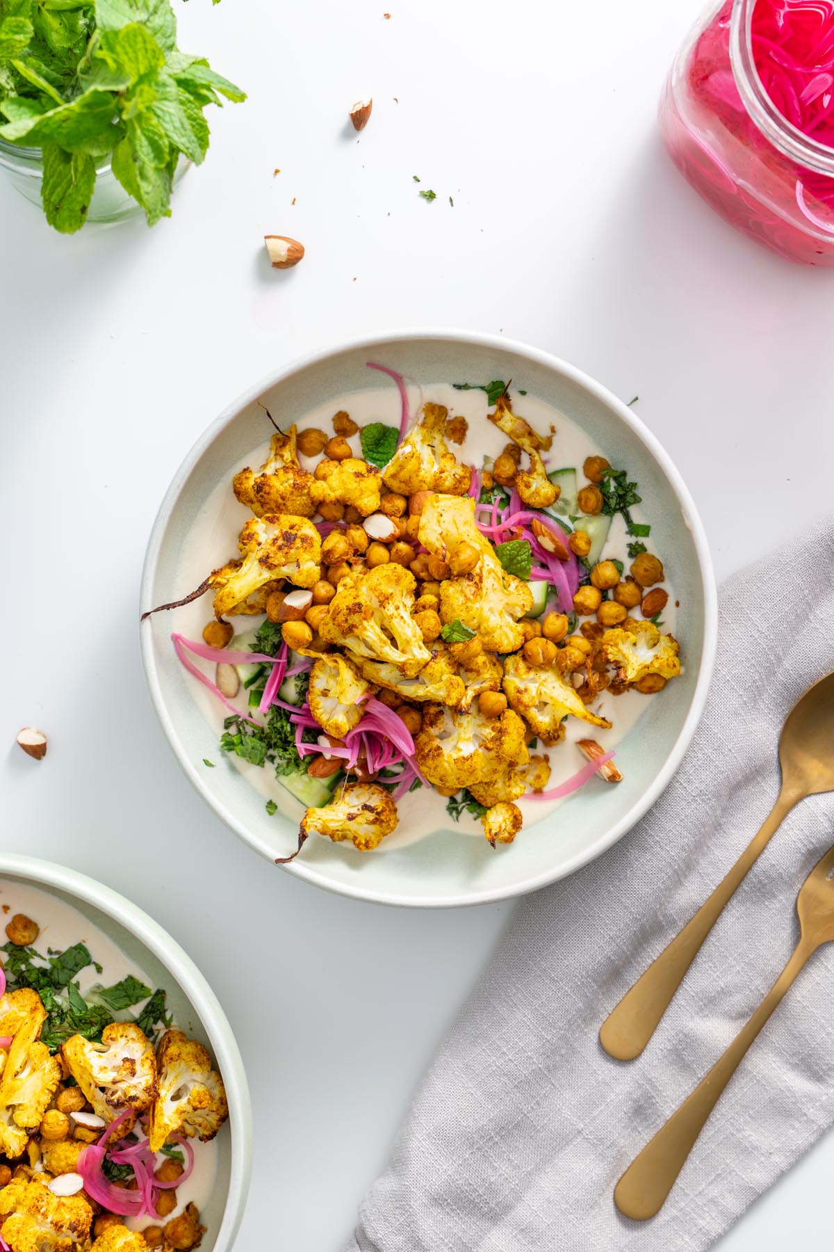 A top-down view of a plated tandoori spiced cauliflower bowl with chickpeas and fresh herbs.