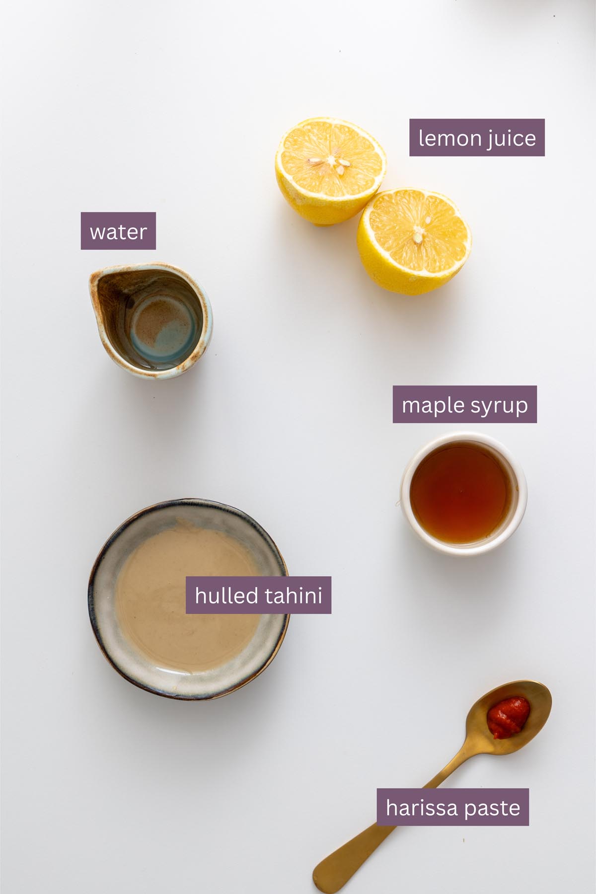 Labeled ingredients for tahini dressing including lemon juice, maple syrup, hulled tahini, harissa paste, and water on a white background.