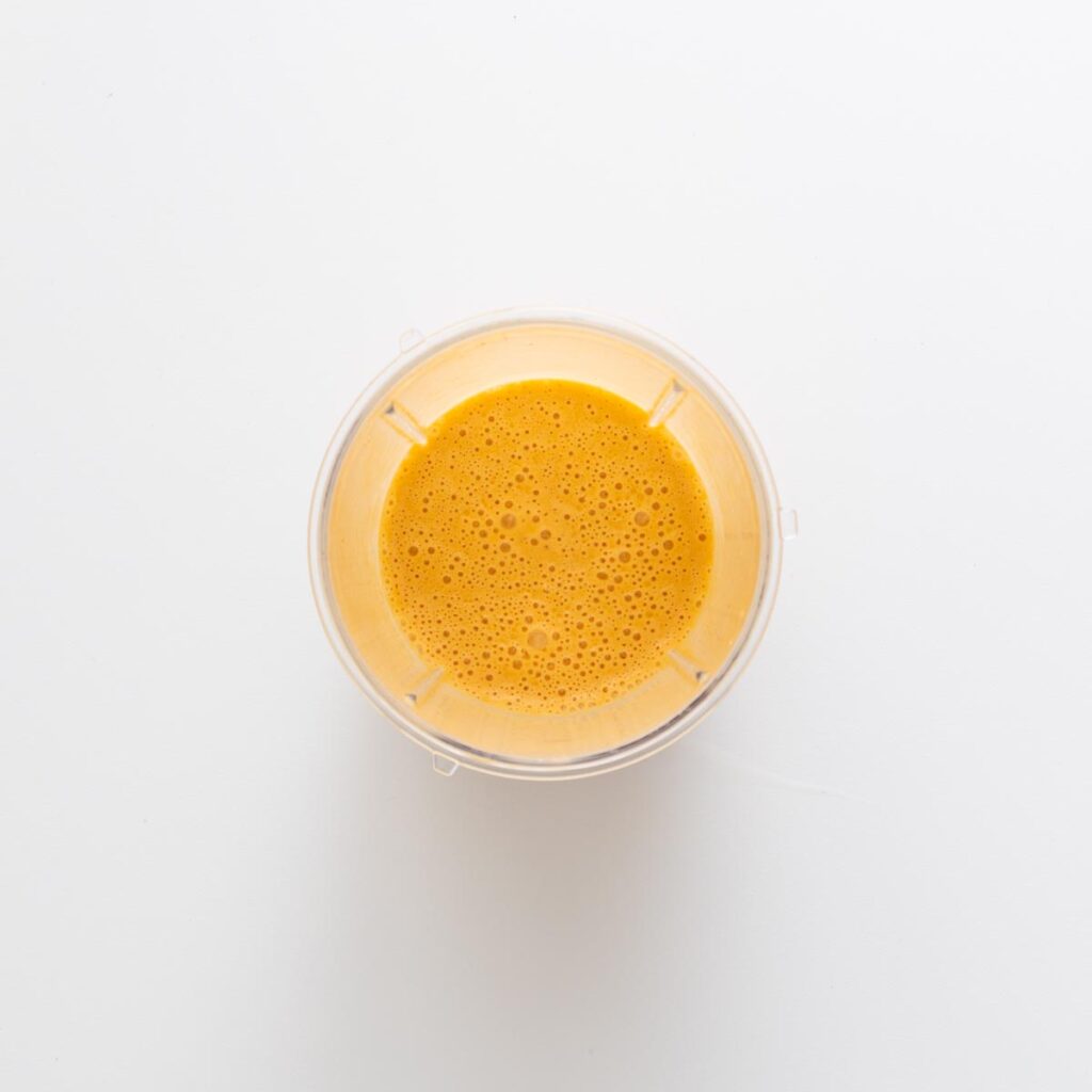 Creamy harissa tahini dressing blended until smooth in a clear blender cup on a white surface.