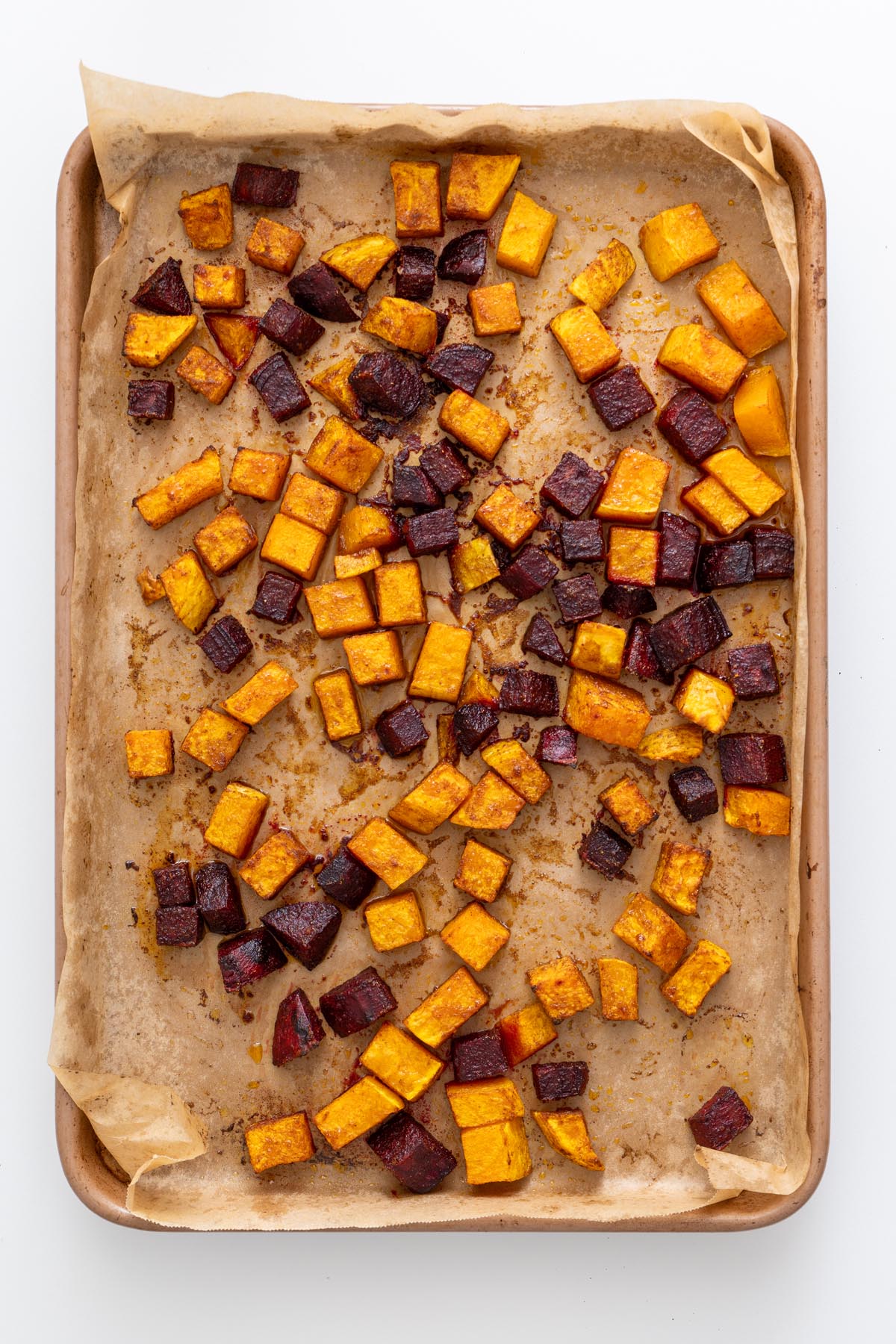 Roasted butternut squash and beet on a baking tray, showing golden edges and caramelization.
