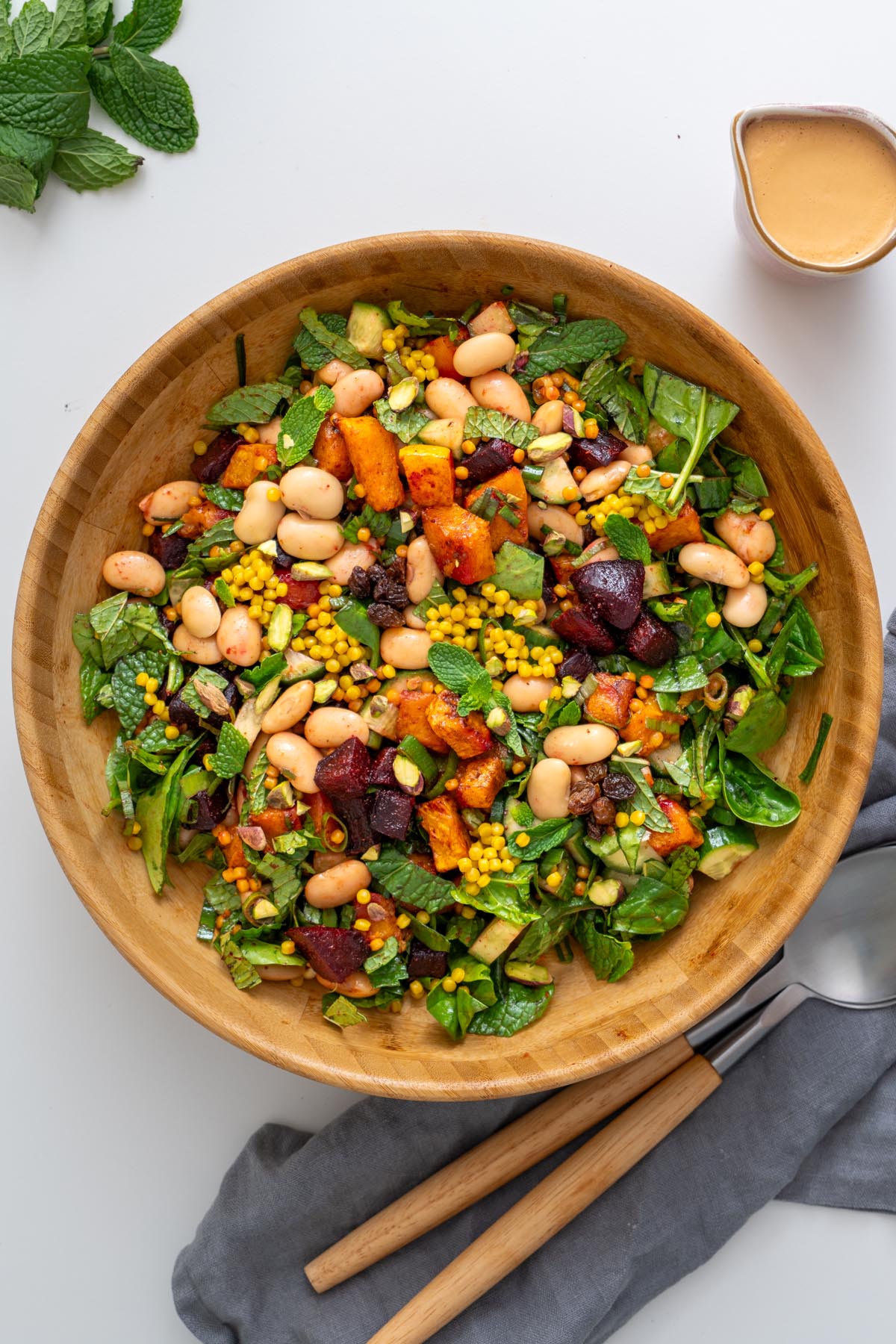 Close-up of Moroccan Spiced Pearl Couscous Salad showing colorful vegetables, couscous, and butter beans in a wooden bowl.
