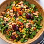 Overhead view of Moroccan Spiced Pearl Couscous Salad in a wooden bowl next to a cup of tahini dressing and mint leaves.