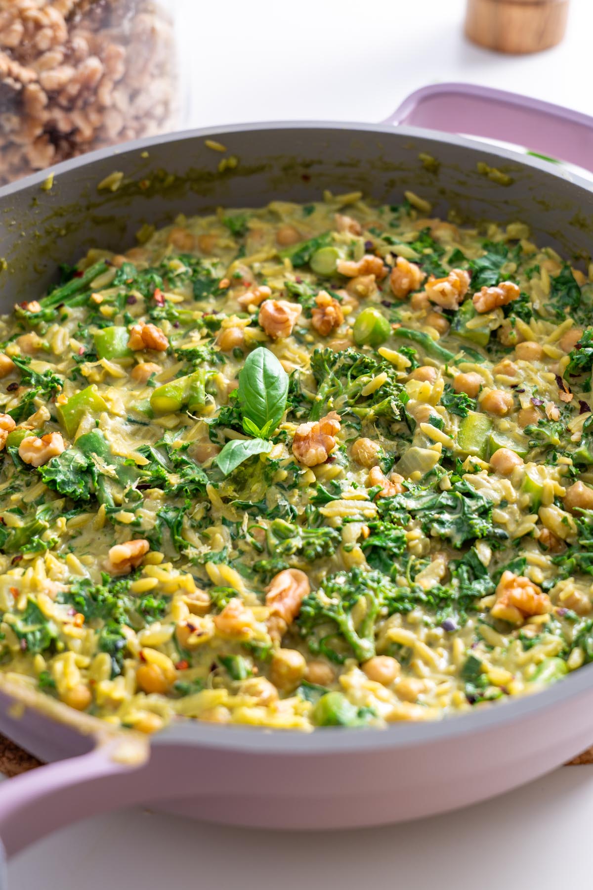 Close-up of finished creamy pesto orzo garnished with fresh basil, walnuts, and chili flakes in a skillet