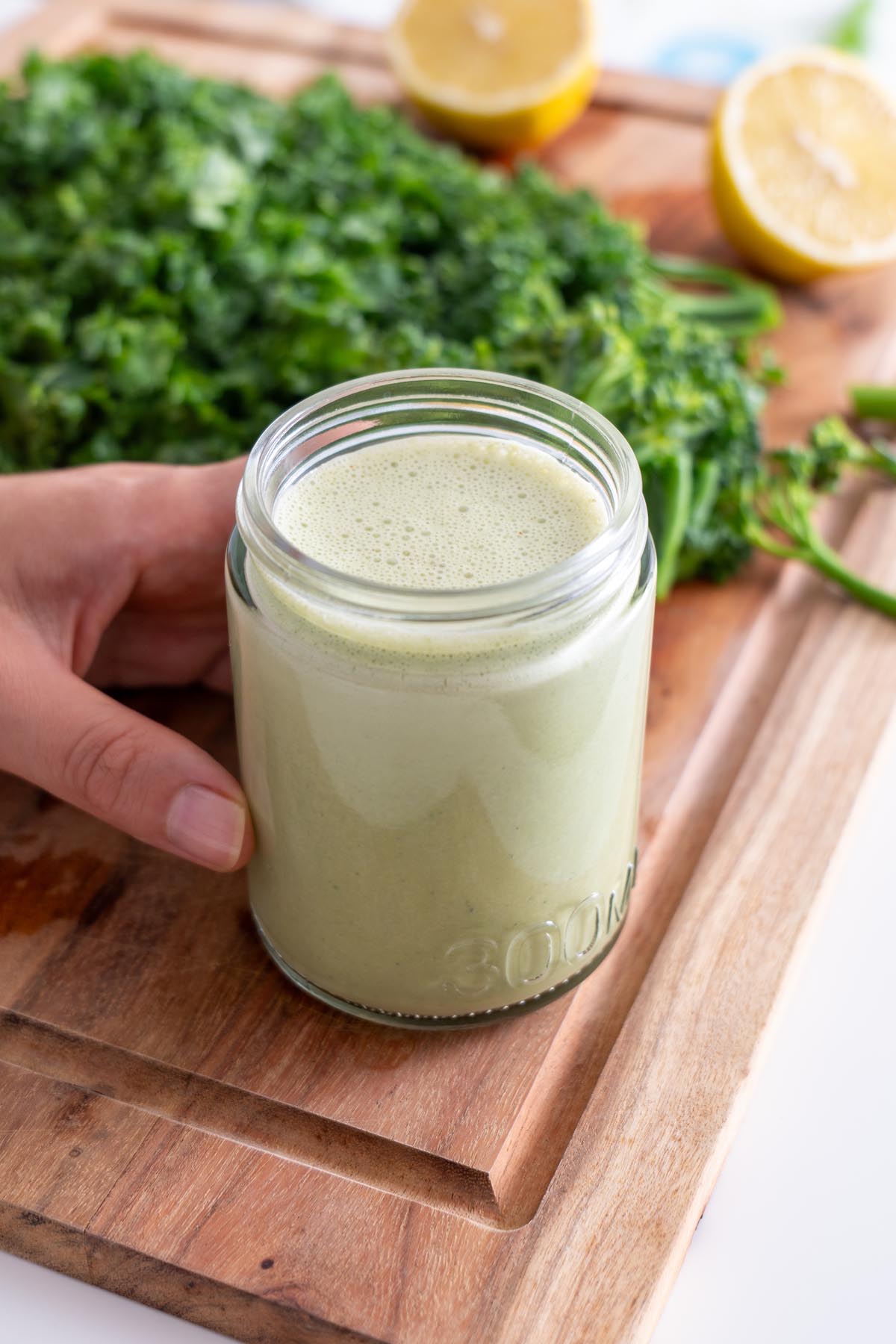 Sarah Cobacho holding a jar of blended pesto sauce for the orzo in front of fresh kale and lemons