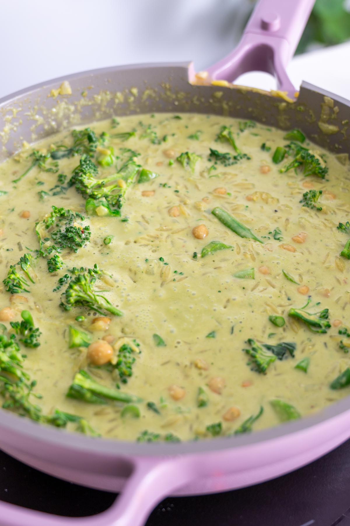 Orzo simmering in pesto sauce with broccolini and chickpeas in a pink skillet before stirring in kale