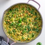 Finished creamy pesto orzo in a pink skillet with wilted kale, chickpeas, broccolini, and walnut garnish