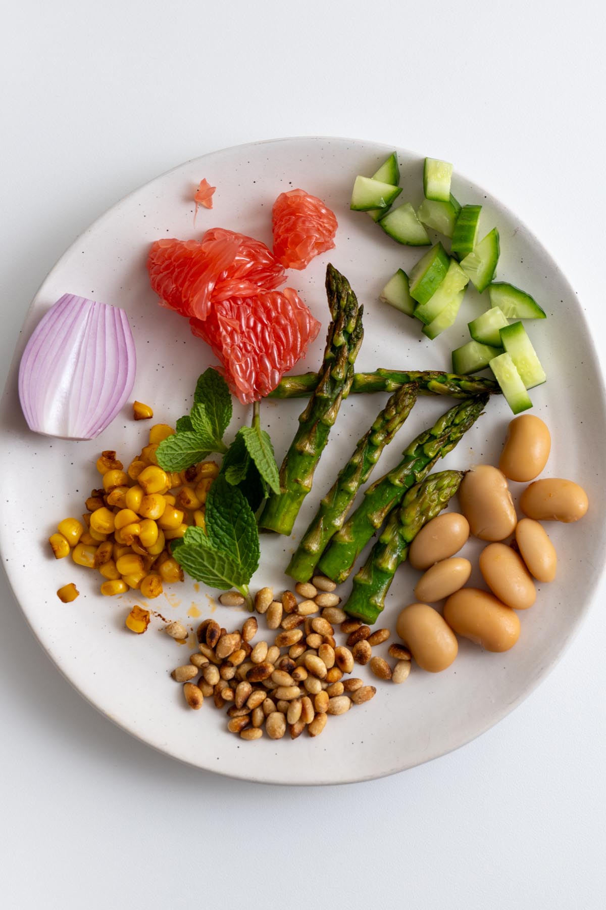 All the primavera salad ingredients arranged on a board, including grapefruit, avocado, mint, and beans