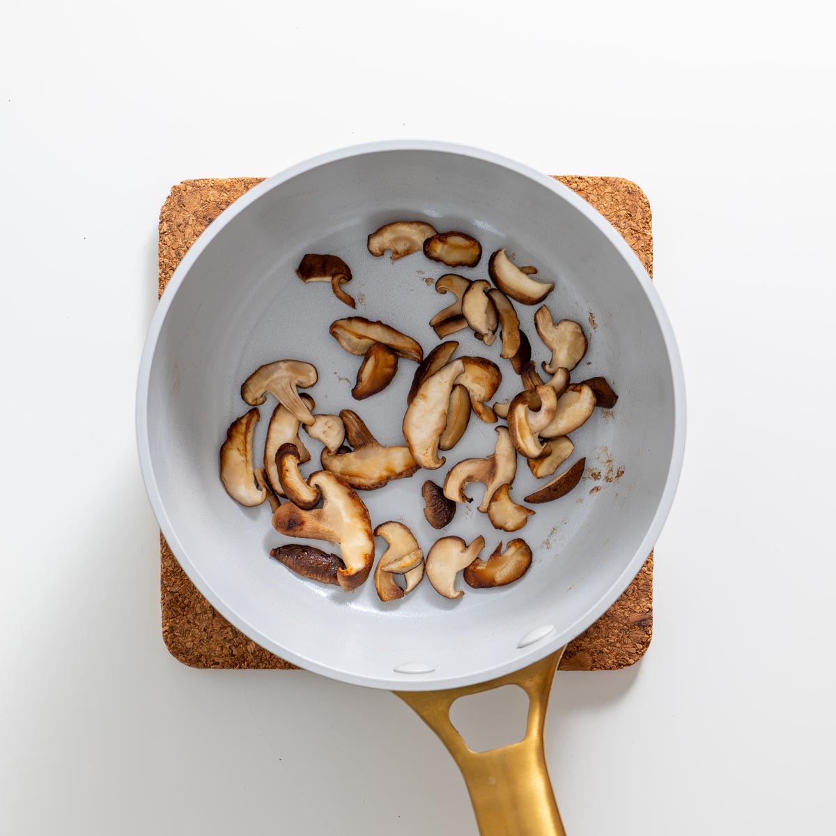 Sautéed shiitake mushrooms in a white ceramic pan on a cork mat