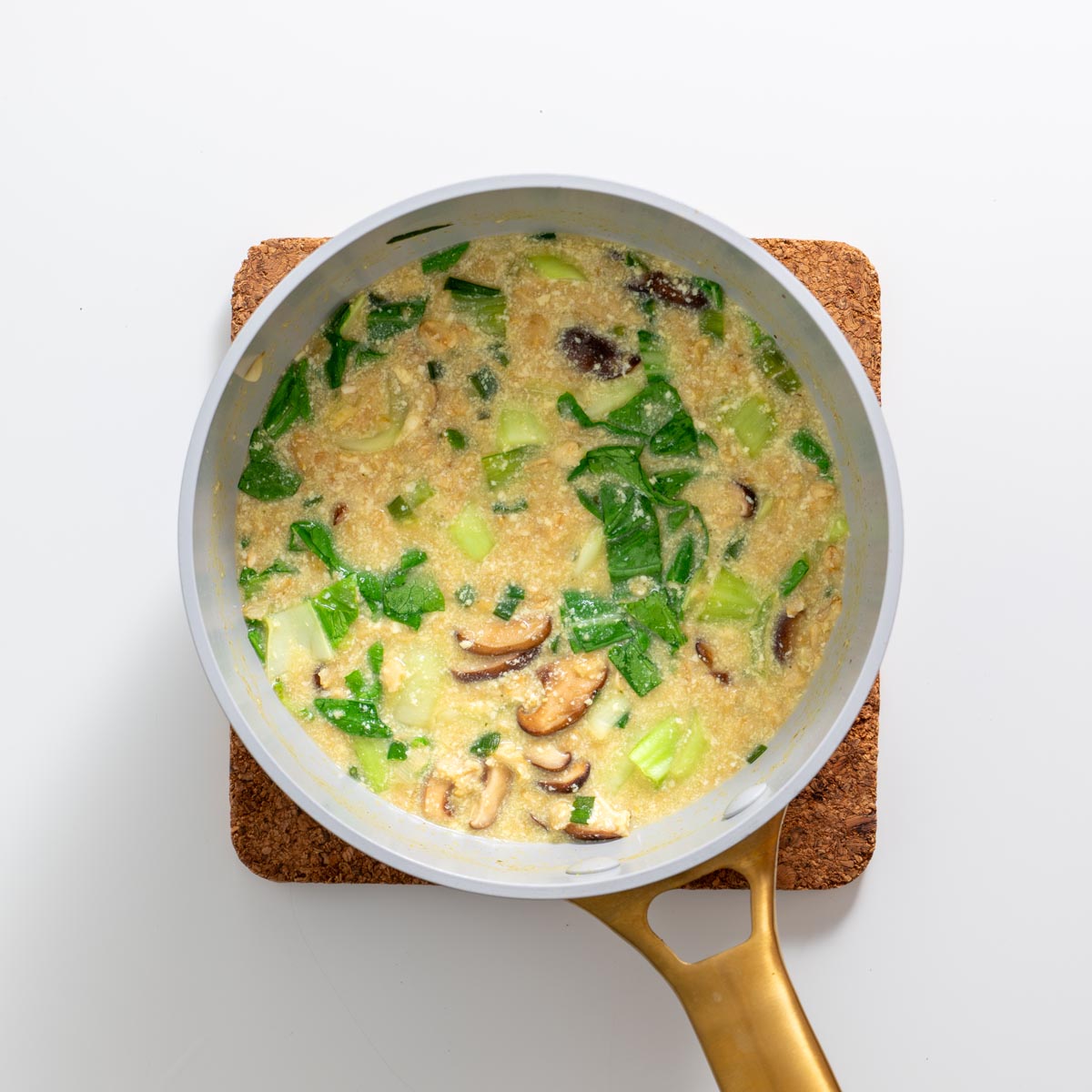 Savory oats simmering in a saucepan with tofu, pak choy, and mushrooms