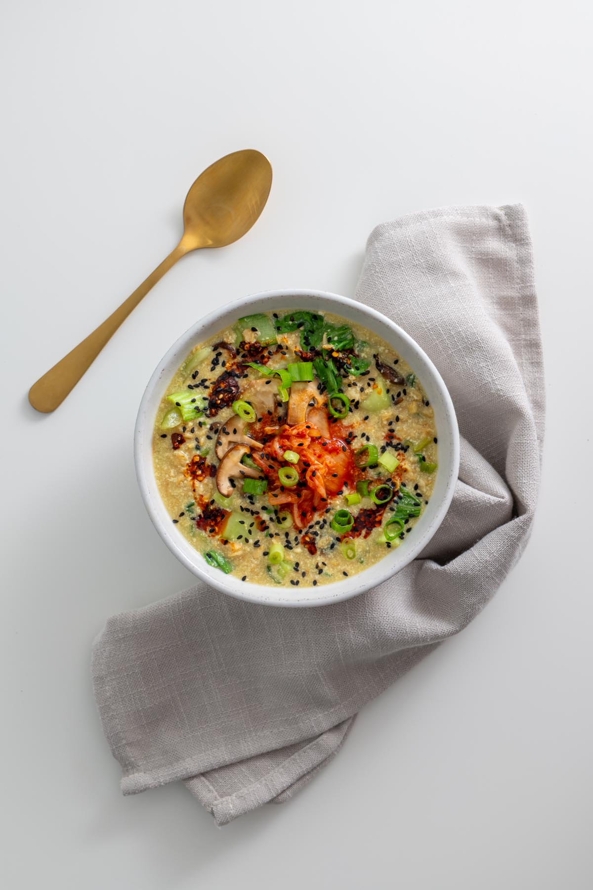 Overhead shot of savory vegan oats topped with kimchi, mushrooms, scallions, and chili oil with a gold spoon on the side