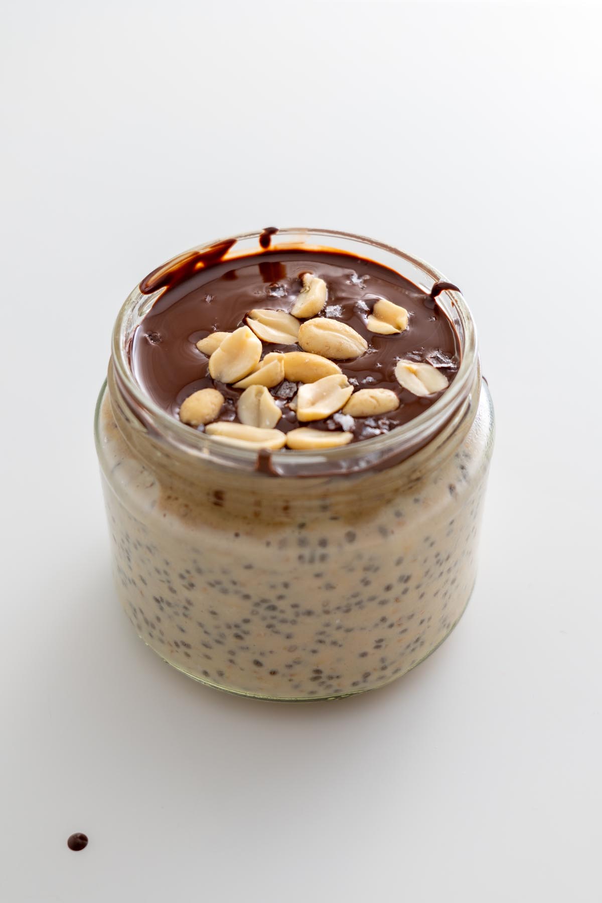 Thick and creamy Snickers overnight oats topped with melted chocolate and peanuts in a glass jar.