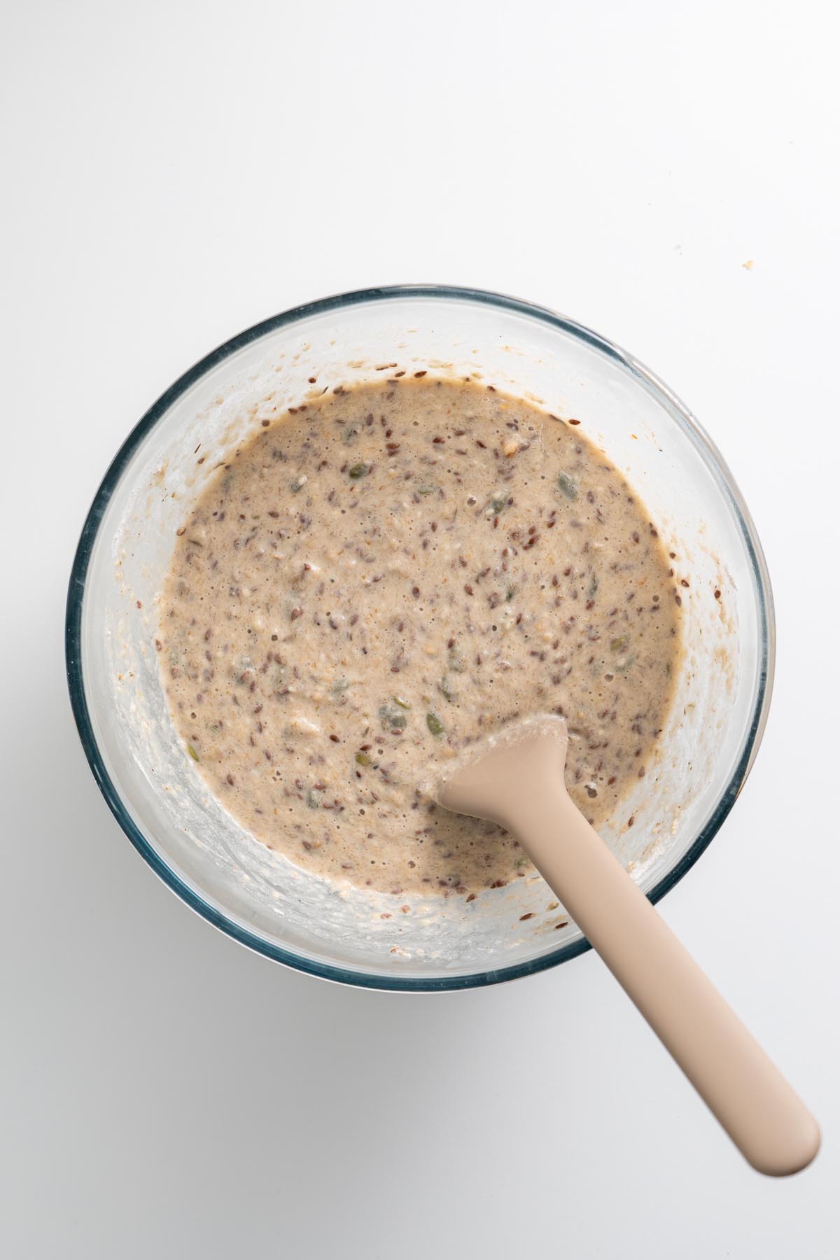 Freshly mixed gluten-free seeded bread batter in a glass bowl with spatula