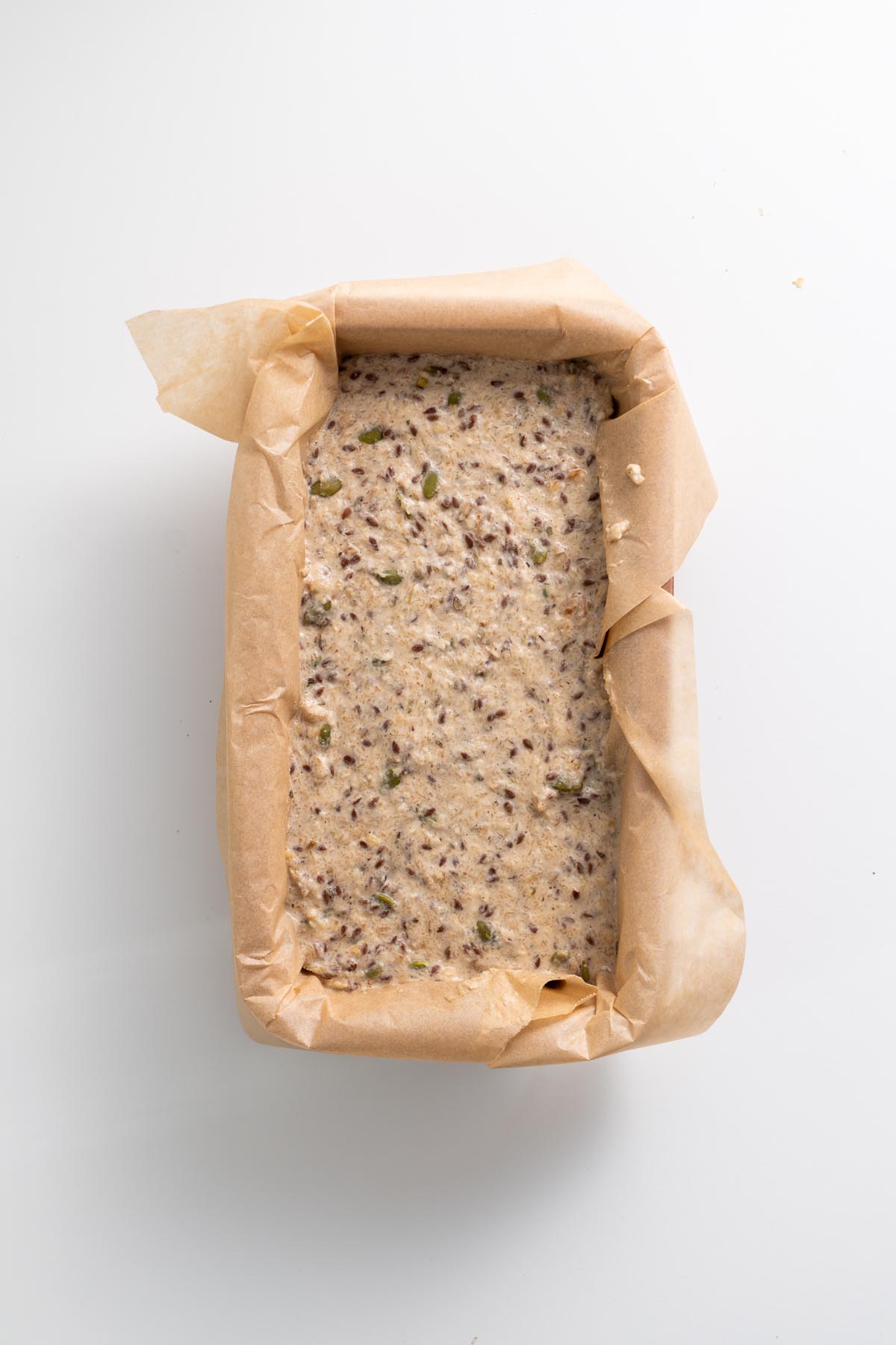 Unbaked gluten-free seeded bread batter in a parchment-lined loaf pan
