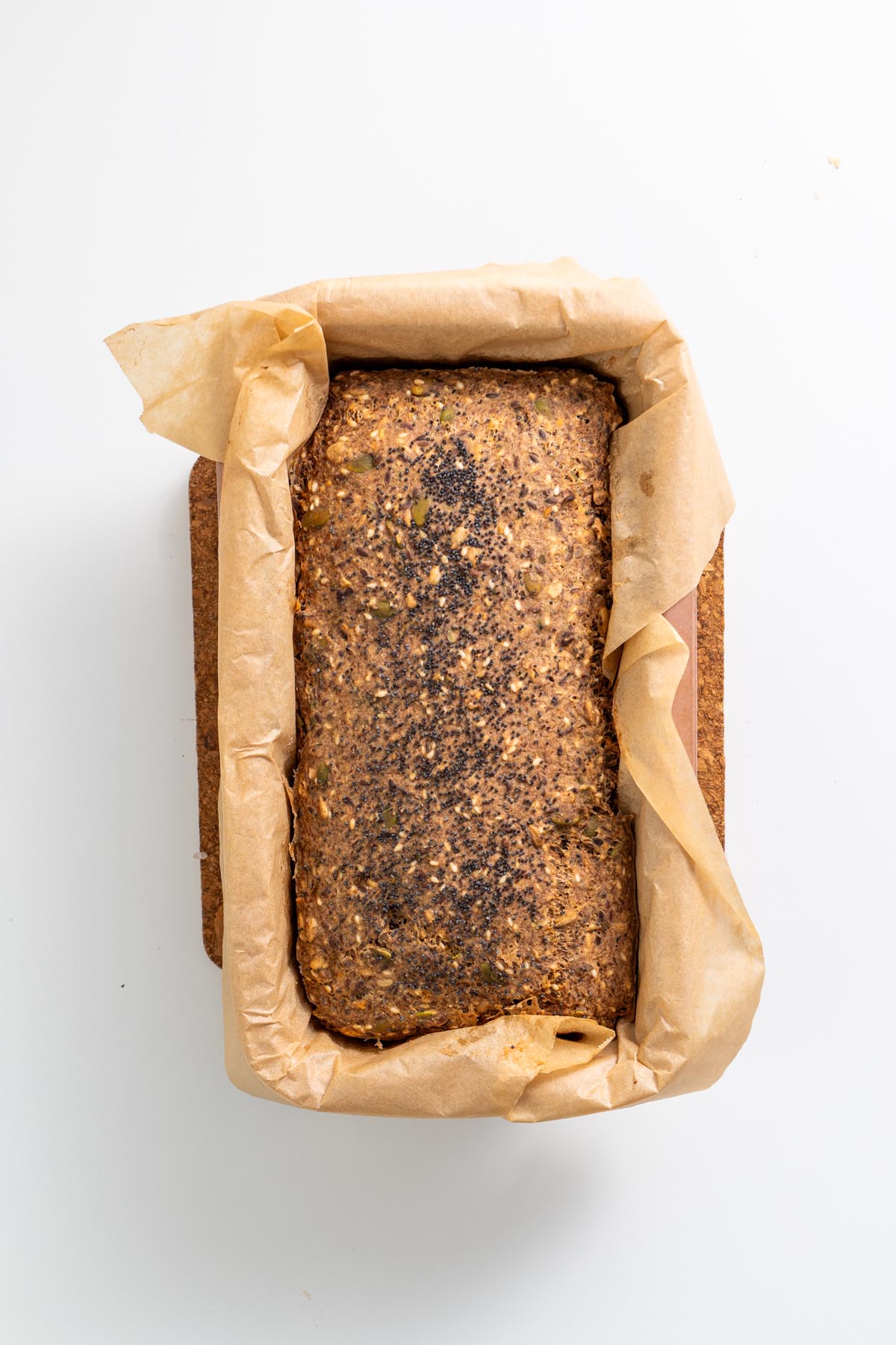 Baked gluten-free seeded bread in parchment-lined loaf pan