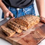 Gluten-free seeded bread being sliced on a wooden board