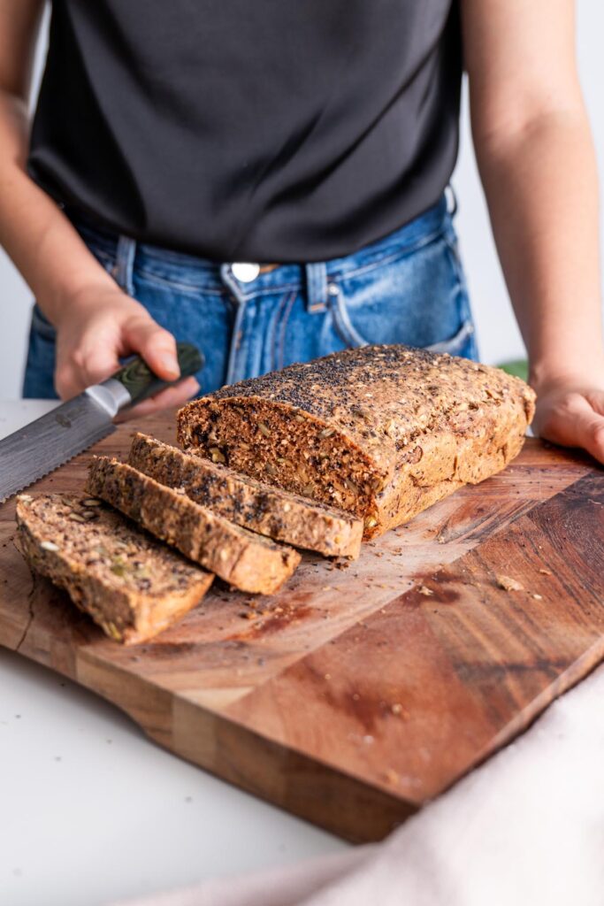 Gluten-free seeded bread being sliced on a wooden board