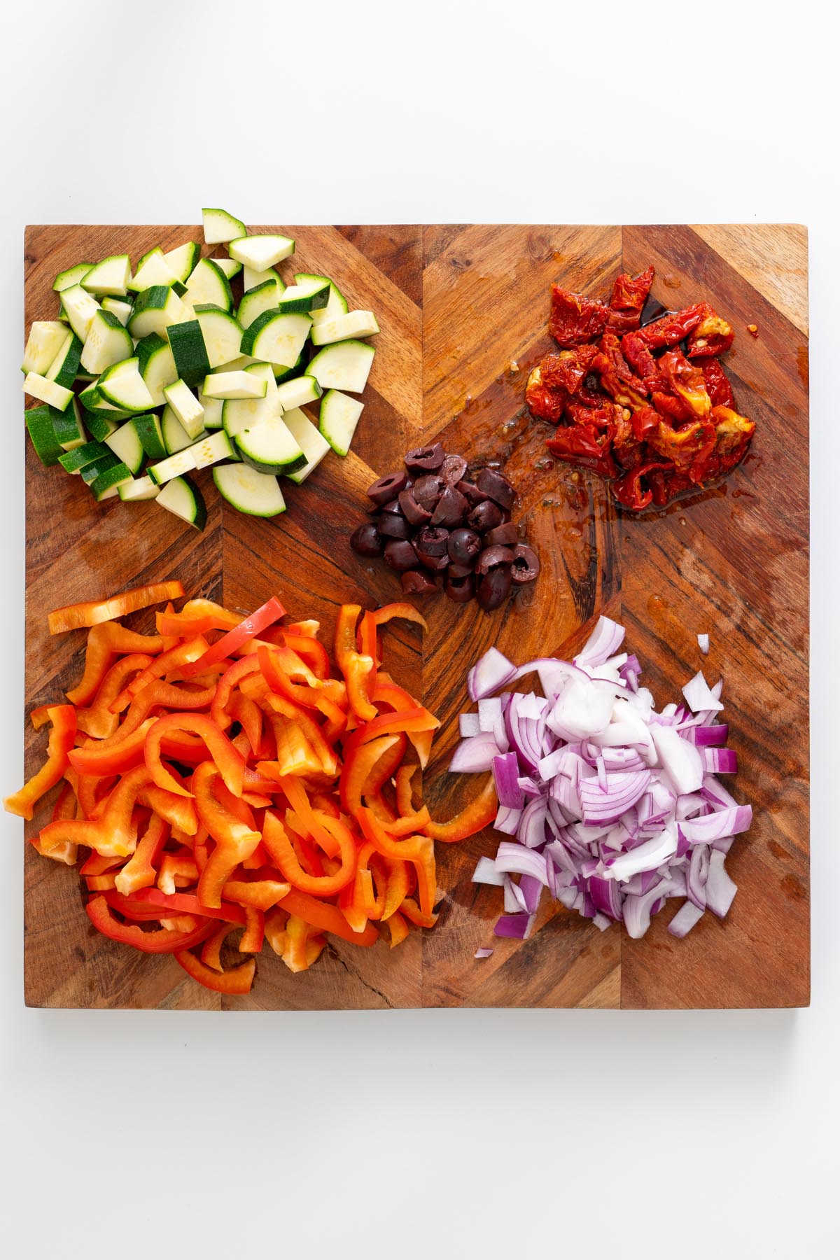 Chopped basil, olives, and sun-dried tomatoes on a board