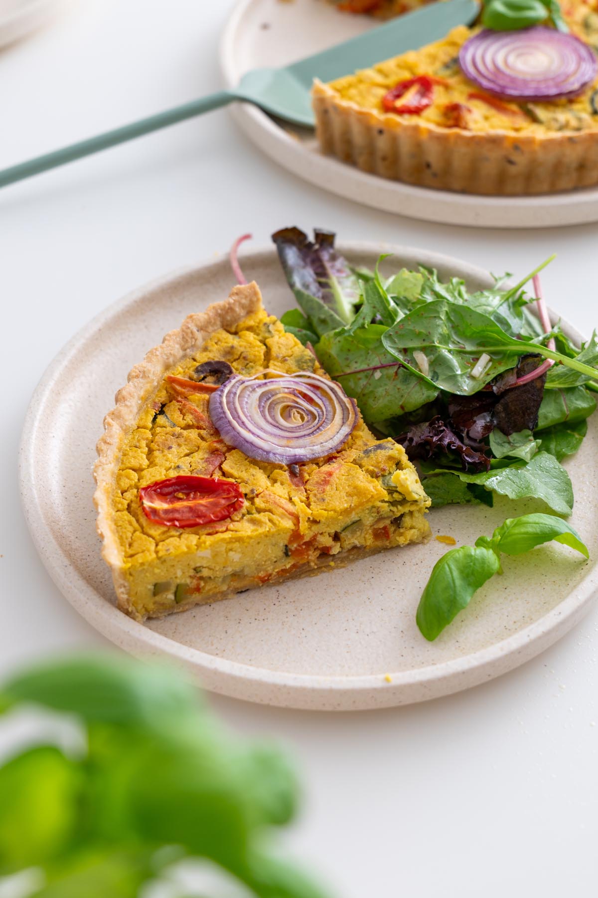 Slice of Mediterranean vegan quiche served with greens on the side