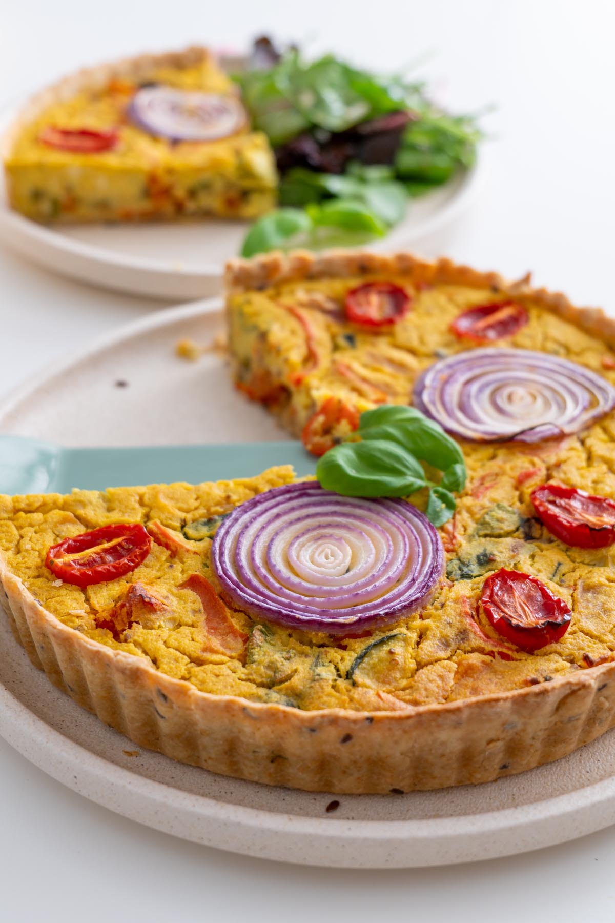 Baked Mediterranean vegan quiche topped with red onion rings and cherry tomatoes