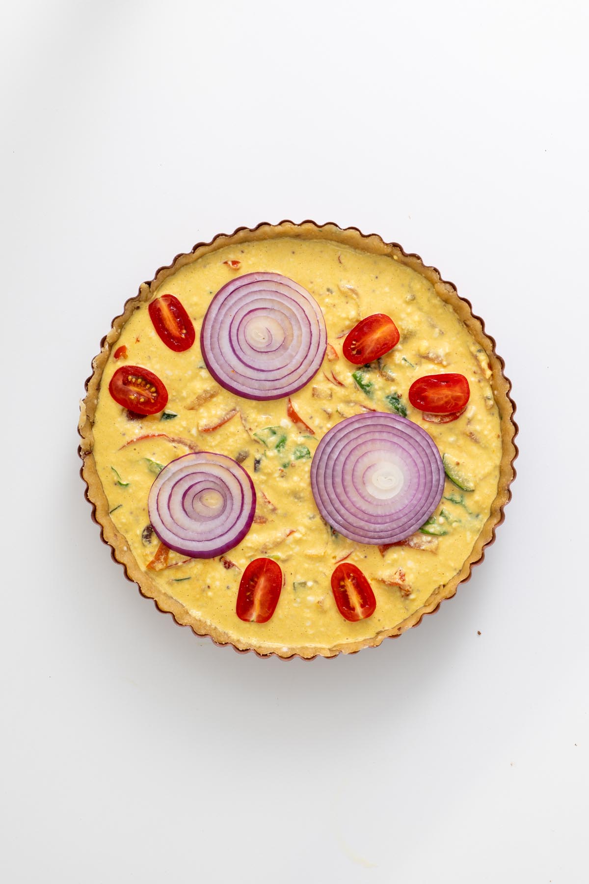 Unbaked quiche with decorative toppings of onion rings and cherry tomatoes