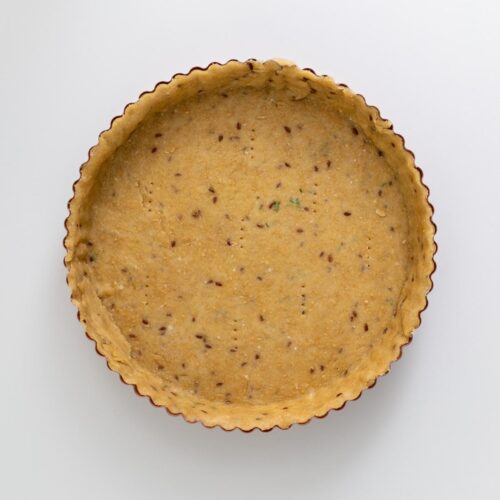 Empty crust pressed into a tart pan with herbs visible in the dough