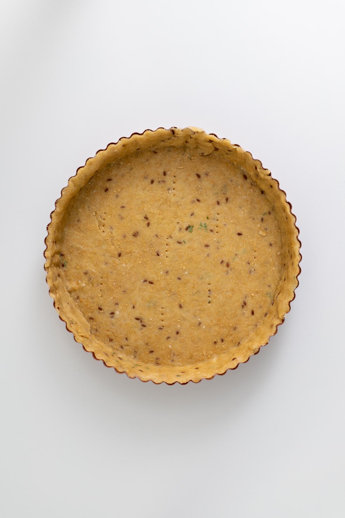Empty crust pressed into a tart pan with herbs visible in the dough