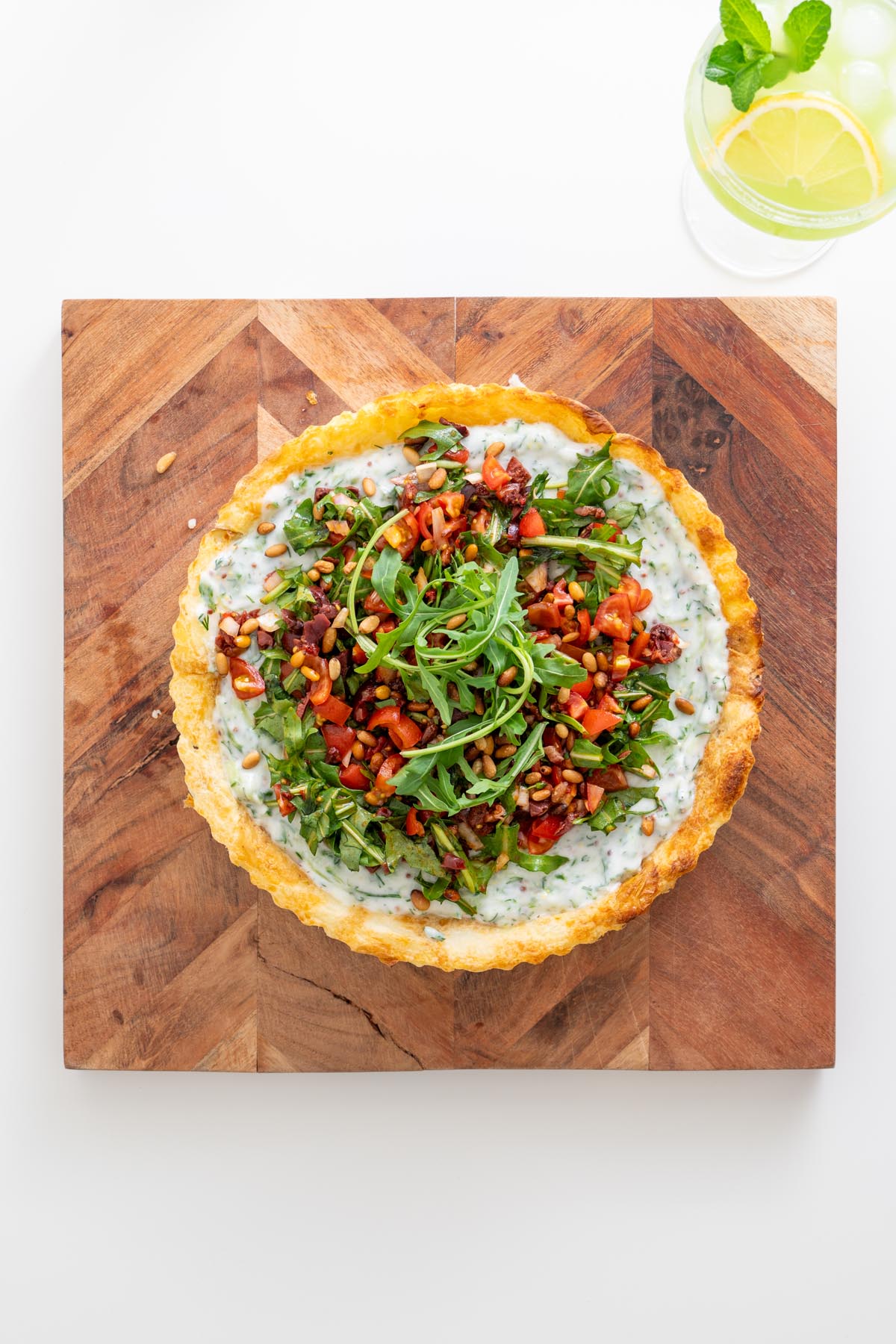 Assembled tart topped with olive mix and arugula on a wooden board