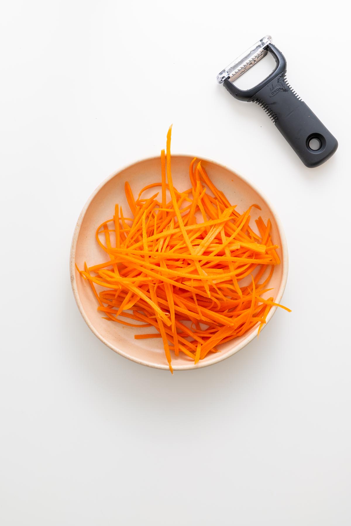 Julienned carrots in a bowl with julienne peeler beside it