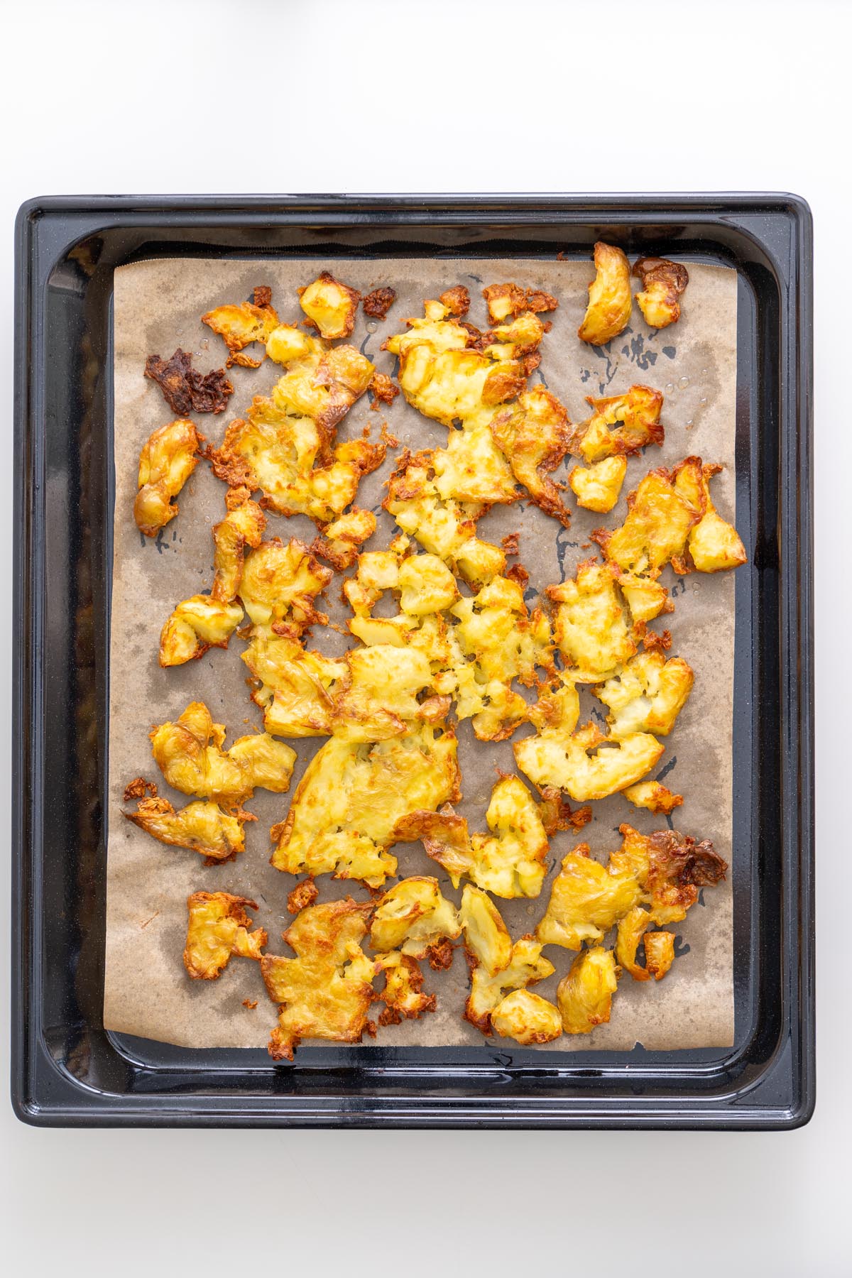 Tray of smashed baby potatoes roasted golden and crispy on parchment paper