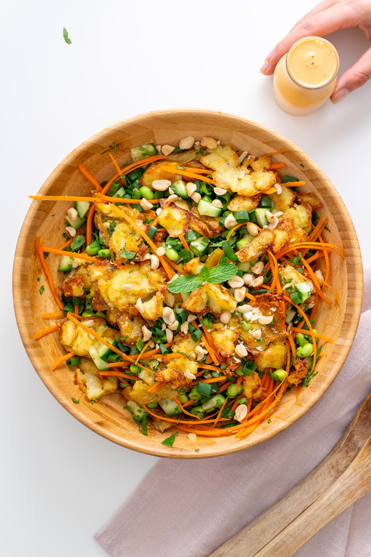 Serving bowl of crispy potato salad with carrots, cucumbers, scallions, and herbs ready to eat