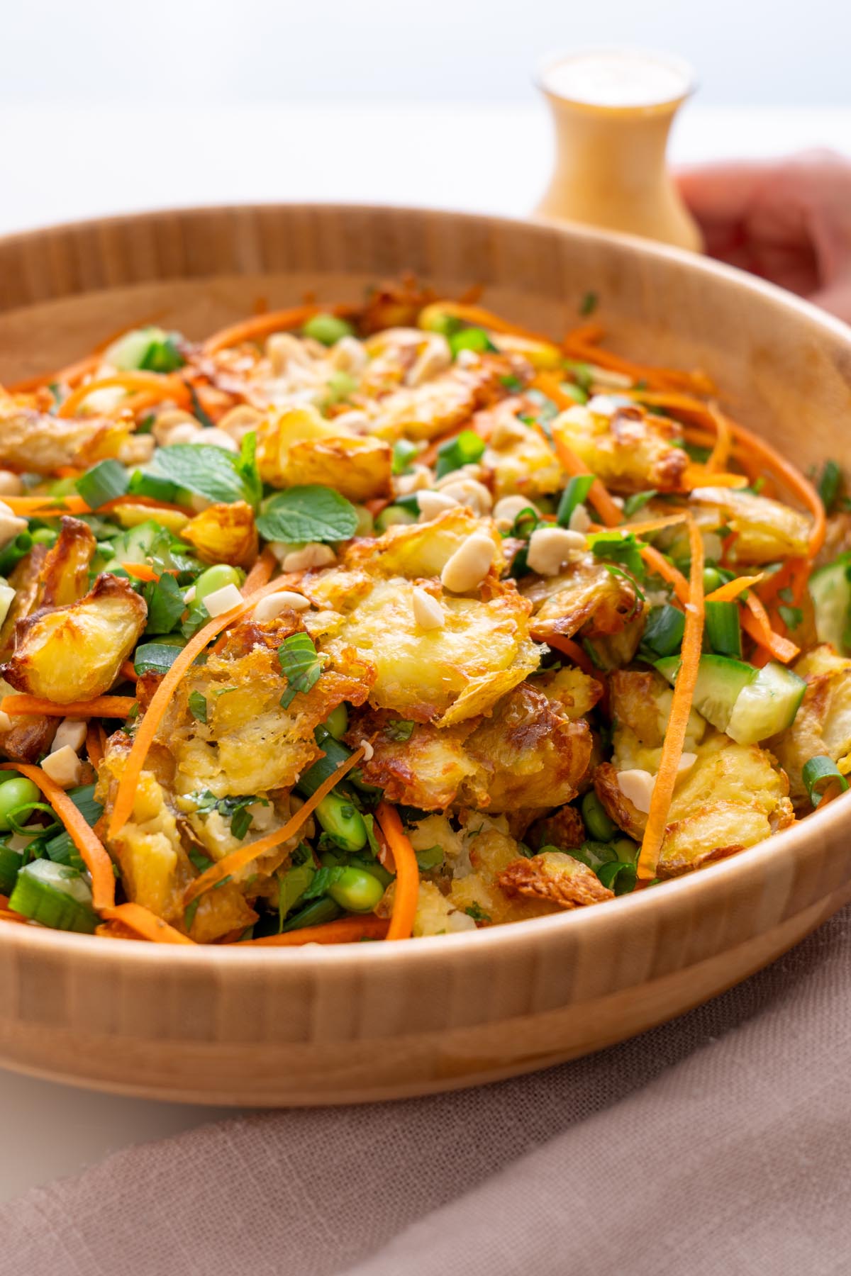 Crispy potato salad ingredients tossed together with herbs, carrot, edamame, and peanuts in a large bowl
