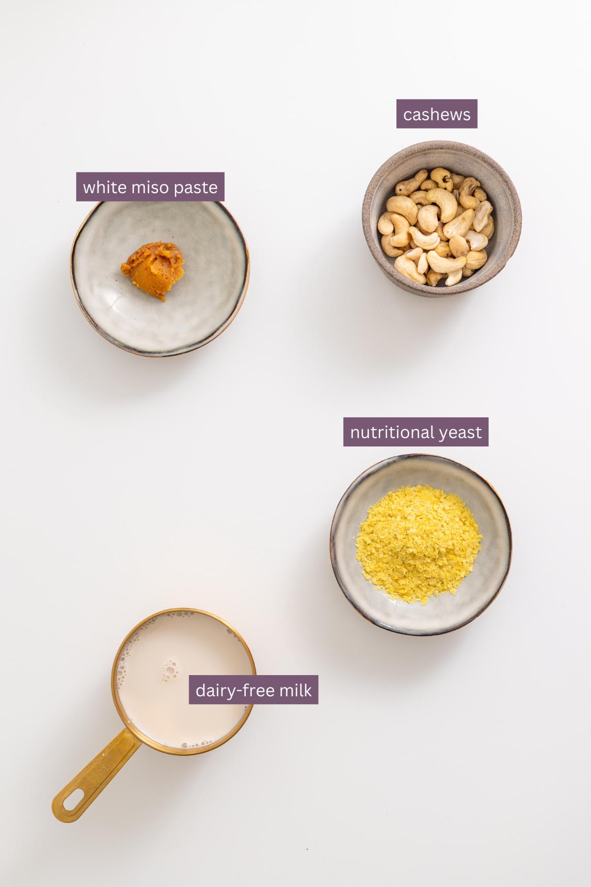 Cashew cream ingredients including cashews, white miso paste, nutritional yeast, and dairy-free milk on a white surface