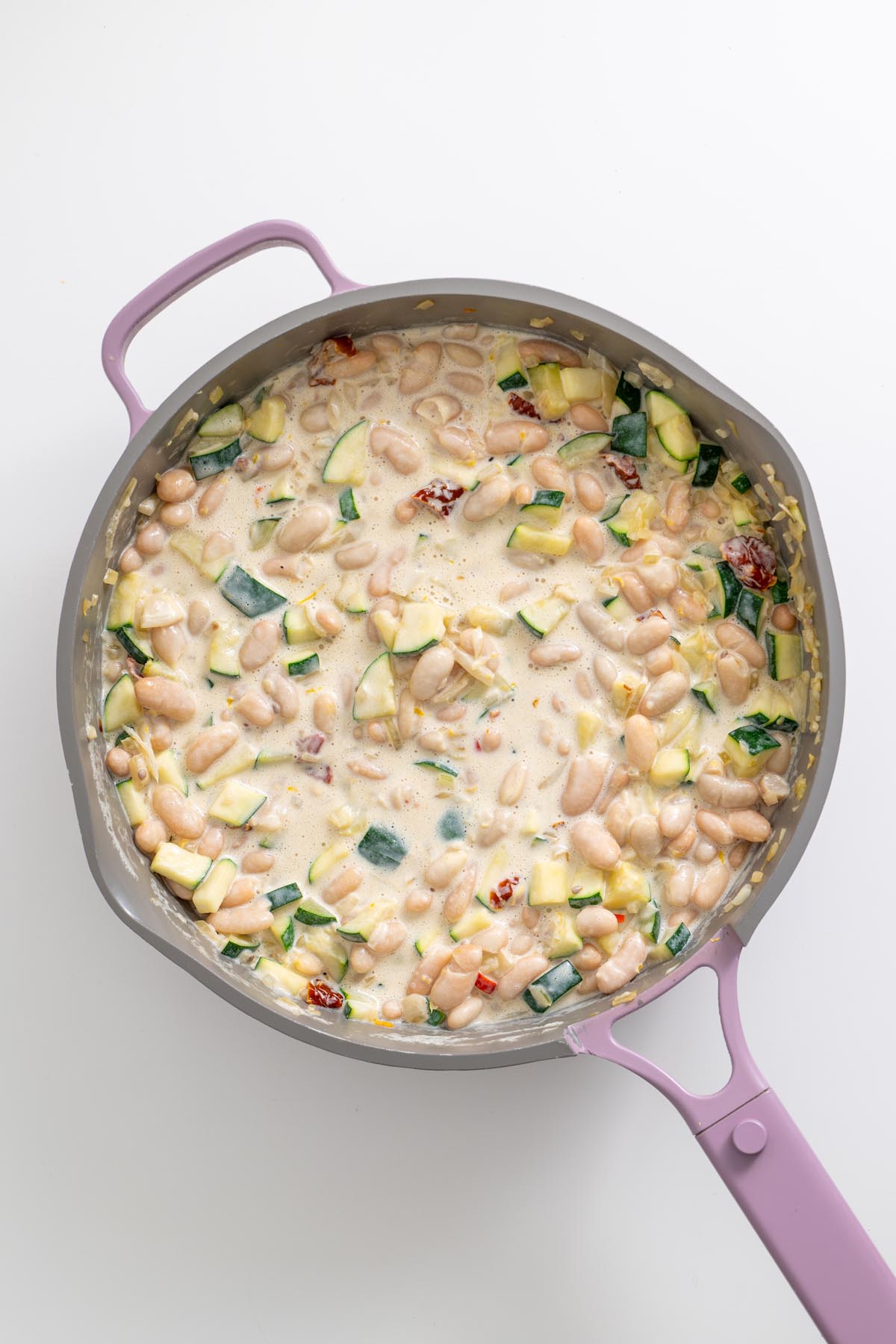 Creamy zucchini and white beans cooking in skillet with sun-dried tomatoes