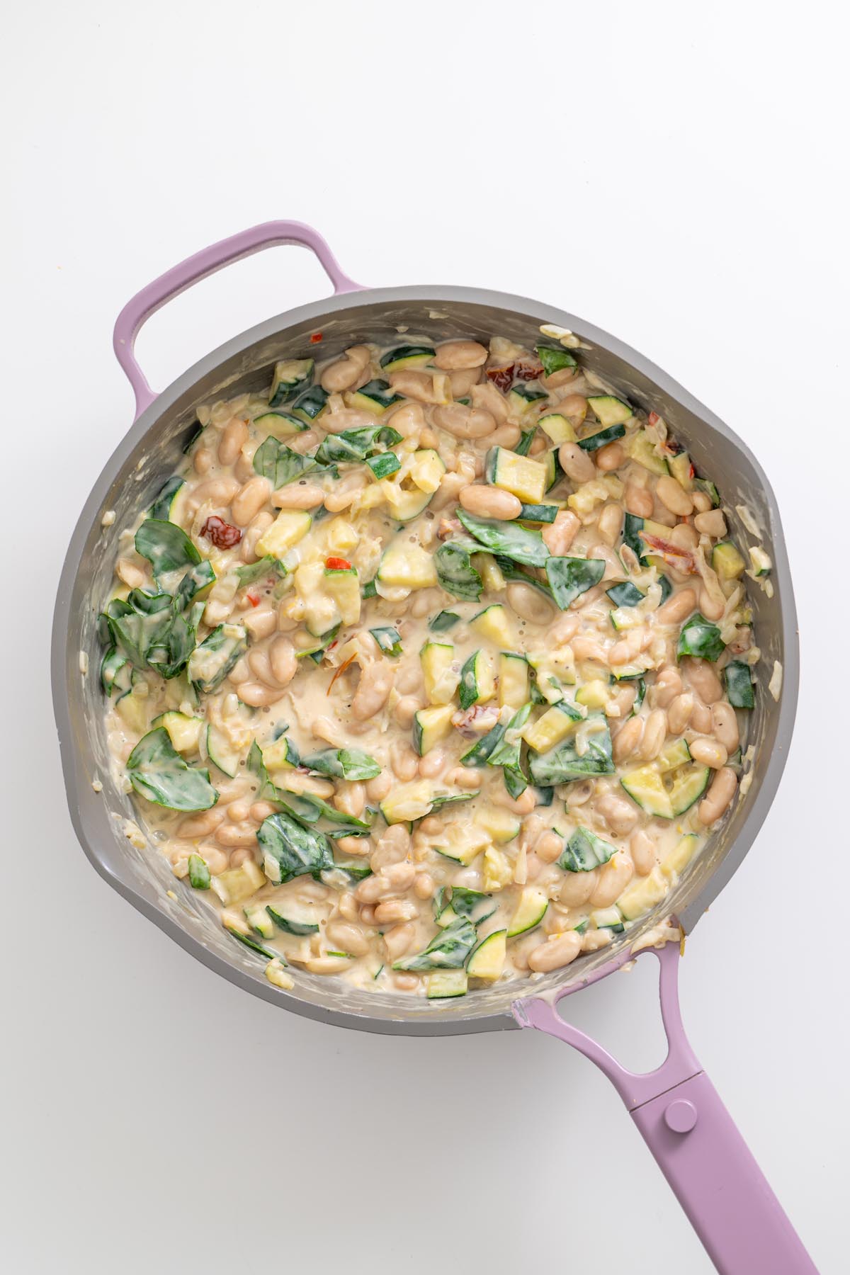 Creamy zucchini beans simmering with fresh greens in skillet
